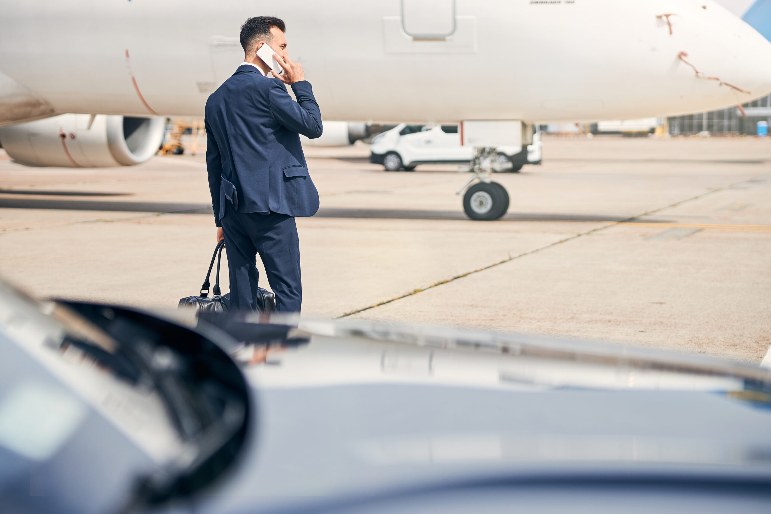 Ambitious brunette man talking on the phone walking towards an aircraft going on a business trip